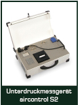 Bild eines Unterdruckmessgeräts, Modell aircontrol S2, in einem geöffneten Koffer. Das Gerät enthält verschiedene Anschlüsse und Bedienelemente, die für die Messung von Unterdruck verwendet werden. Der Koffer ist metallic und hat eine helle Innenseite.