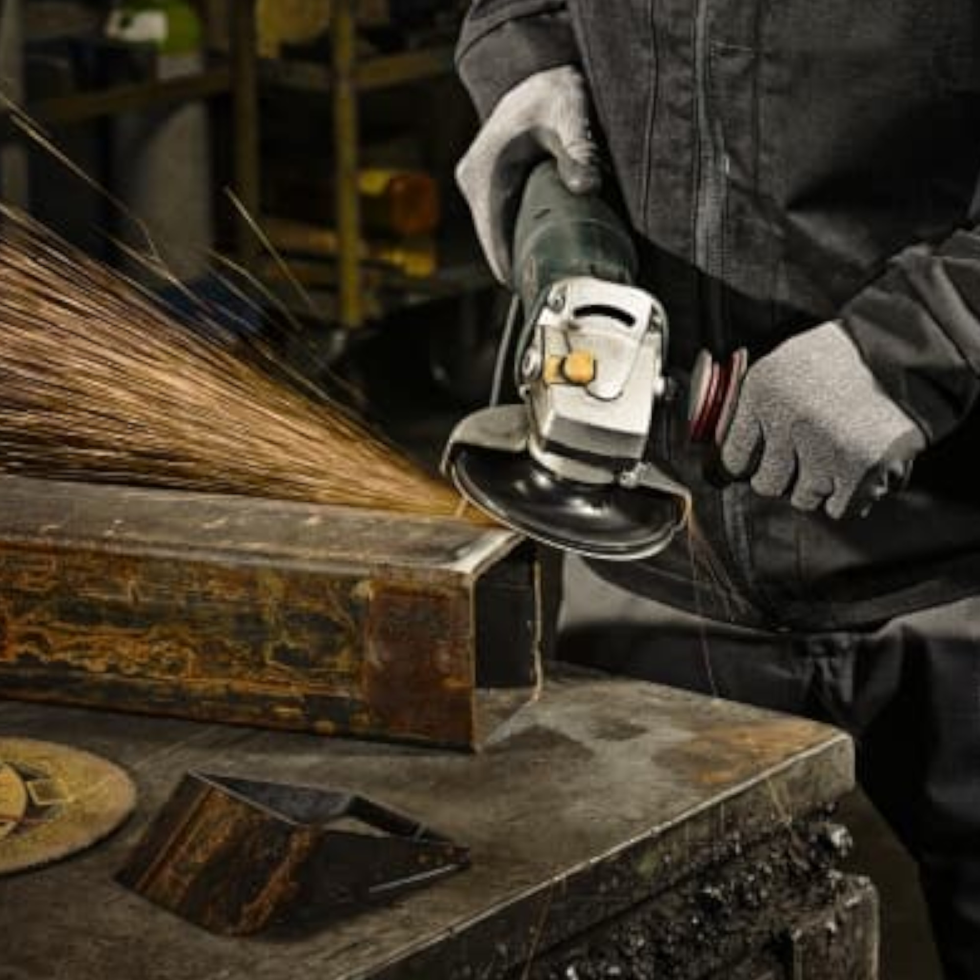 Ein Handwerker hält einen Winkelschleifer, während Funken von einem Metallstück sprühen. Der Arbeiter trägt Handschuhe und steht an einem Werkbank, um metallische Bearbeitungen durchzuführen. Im Hintergrund sind weitere Werkzeuge und Materialien sichtbar.