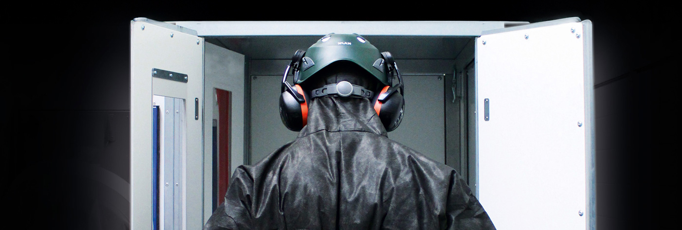 Person mit Schutzhelm und Gehörschutz betritt industrielle Kammer