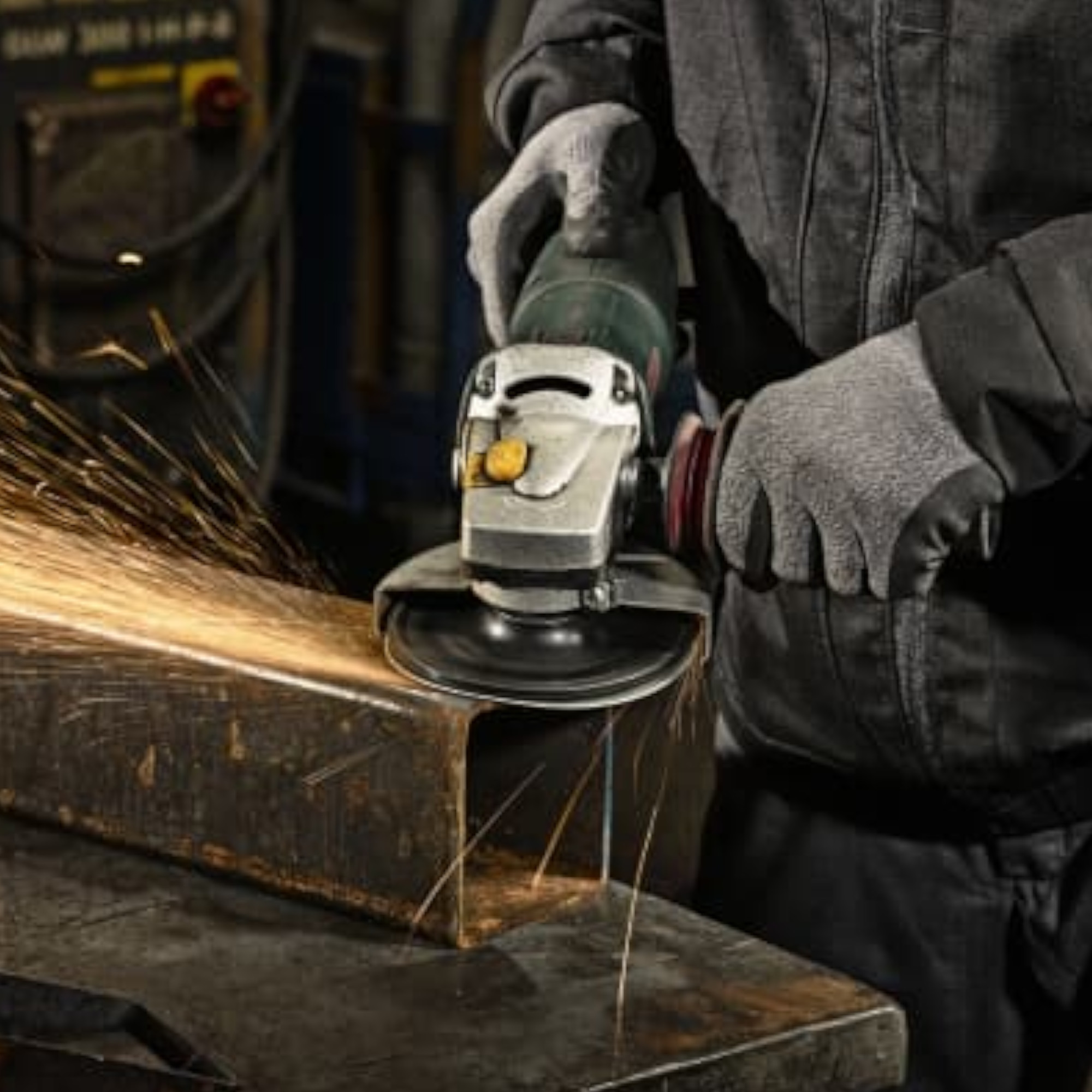 Eine Person trägt Arbeitshandschuhe und hält eine Winkelschleifmaschine, die Funken erzeugt, während sie an einem Metallstück arbeitet. Die Umgebung ist industriell geprägt und vermittelt eine aktive Arbeitsatmosphäre.
